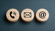 © Chloe - Three round wooden blocks arranged in a row featuring black contact icons: telephone receiver, envelope mail, and at symbol representing communication methods and customer support