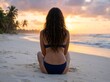 © Vasiliy - Back view of a woman sitting on a tropical beach at sunset. Female tourist relaxing on the sand looking at the ocean. Summer vacation getaway