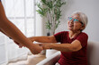 © David - Senior adult woman sitting on a sofa and happily holding hands with a caregiver, receiving support and assistance in her daily living at home