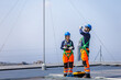 © JU.STOCKER - Two solar engineers in safety uniform and harnesses working on rooftop solar farm, Maintenance team of technicians inspecting solar panels installation on industrial solar roof under blue sky