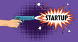 © Protik - Hand holding a pistol firing a shot that results in a comic book explosion with the word STARTUP on a vibrant purple background.