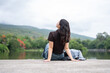 © bongkarn - Back view of asian woman chilling beside lake across mountain while sitting on concrete road ground.