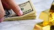 © olga_demina - A close-up view of a hand holding a stack of US dollar bills next to gold bars on a marble surface, representing a secure and stable investment strategy for wealth management and financial growth.