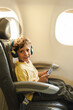 © SISMIZ - Young boy traveling by airplane using headphones and phone