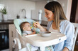 © SISMIZ - Mother feeding baby solid food in high chair