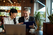 © Marko Geber - Two colleagues reviewing documents with laptop in a modern cafe