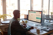 © Seventyfour - African American young adult man managing digital calendar on desktop computer in modern office, planning schedule and productivity. Ideal for remote work, time management, planning