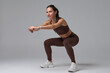 © Sergey Mironov - Fit woman doing squatting exercise looking at camera on gray background