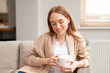 © Iryna - Young woman enjoys coffee while sitting on a couch in a bright room during the afternoon hours