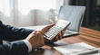 © Rahman - Business professional using calculator with financial icons floating above on a wooden desk in office