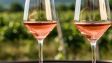 Two Elegant Wine Glasses Filled With Refreshing Pink Rosé Wine, Set Against a Blurred Vineyard Landscape