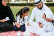© oneinchpunch - Arabian family in traditional dress smiling together on a picnic blanket in a sunny green park, parents and children enjoying leisure, bonding and relaxation outdoors