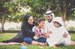 © oneinchpunch - Arabian family in traditional dress smiling together on a picnic blanket in a sunny green park, parents and children enjoying leisure, bonding and relaxation outdoors