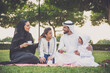 © oneinchpunch - Arabian family in traditional dress smiling together on a picnic blanket in a sunny green park, parents and children enjoying leisure, bonding and relaxation outdoors