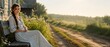 © Nikolay - Beautiful young woman with long braid sitting on wooden bench near village house, scenic countryside road at sunrise