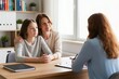 © miss irine - Mother and daughter talk with counselor during therapy session. Psychologist listens carefully, taking notes. Family discusses problems at therapy office. Mental health support.