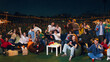 © master1305 - Excited crowd of friends celebrating outdoor sports viewing party at night. Concept of fan zone, live match broadcast, youth gathering, summer night leisure and event promotion.