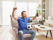 © Ljupco Smokovski - Football fan sitting in an armchair with a beer and celebrating
