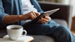 © Mary - Person using digital tablet on sofa at home with coffee cup in foreground.