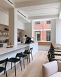 © AI for you - Minimalist modern cafe interior featuring a barista preparing coffee at a sleek counter with wooden accents and large windows overlooking a brick building