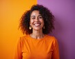 © Viktor - Middle aged hispanic woman with curly hair smiles broadly. She wears an orange shirt against a vibrant orange and purple background. Her expression is joyful and confident.