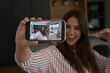 © simona - Excited woman recording a selfie video on her smartphone while holding house keys in new home