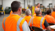 © A2Z AI  - Rear view of adult male employees in bright orange safety vests attentivly participate in a workplace seminar, focused on a speaker or presentation in a diverse group in a professional industrial envi