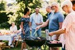 © Juan - Multigenerational family cooking barbecue together outdoors
