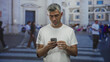 © Krakenimages.com - Man with grey hair holding smartphone, left palm up in questioning gesture, looking at screen on a busy street; frustration isolation.