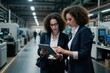 © Pete - Two women in business suits analyze data on a tablet inside a modern factory. They collaborate, discussing production strategies and planning for manufacturing efficiency and innovation.