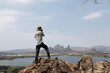 © SHUTTER DIN - Male Photographer Standing On Mountain Summit Overlooking A Vast Lake And Valley During A Clear Day