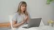 © Krakenimages.com - Woman on bed with laptop, hands gesturing and speaking in a building bedroom; online support concern.