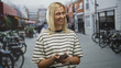 © Krakenimages.com - Woman holding smartphone smiling on a city street beside bicycles and cafes; contentment social connection.