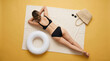 © Cliff - Top view from behind of a beautiful young woman in a stylish monochromatic bikini lying on a beach blanket with an inflatable ring against a bright yellow background