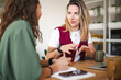 © Studio Marmellata - Two women are engaged in a discussion at a table, one taking notes while the other gestures with her hands.