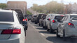 © thongchainak - Long line of cars stuck in a traffic jam on a bright day. Perspective is from behind a white sedan. Showing the vast number of vehicles extending into the distance on a multi-lane road.