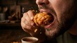 © Adjie - Close-up of a man taking a bite of a crispy fried chicken drumstick with sauce.