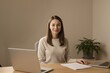© Michael - A woman in a light beige sweater sits at a wooden desk, surrounded by laptops and papers, exuding a calm professional atmosphere amidst soft natural lighting.