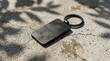 © Iwan.creates - Blank black metal keychain mockup on concrete floor with leaf shadows, rectangular metallic key ring template for branding presentation, high angle view