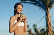 © SHOTPRIME STUDIO - Young woman in a white bikini enjoying a refreshing drink from a coconut outdoors on a sunny day, with palm trees behind, embodying carefree tropical lifestyle and summer wellness.