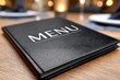 © whitestorm - Elegant black restaurant menu cover with white text 'MENU' on a wooden table.