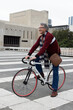 © wavebreak3 - Senior man smiling, pausing on white bicycle at plaza, wearing maroon sweater, carrying leather bag