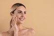 © Anastasiya - Smiling young caucasian woman with radiant healthy skin touching cheek in beauty and skincare concept isolated on clean beige studio background, copy space