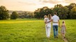 © Ada - Rear view. Happy family with children walking in the park. Happy young family with two children walking together in green park from behind, back view family lifestyle concept with wide copy space