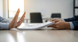 © Elenba - Person refusing to accept documents or contract from another person across a table, symbolizing rejection or disagreement in business negotiations or legal matters.