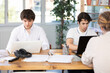 © JackF - Young and adult men sit at desks in office, focused on laptop screens while working during daytime