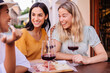 © Xavier Lorenzo - Multiracial women laughing while drinking red wine at outdoor cafe. Young female friends enjoying relaxed social time in European city. Lifestyle and friendship concept.