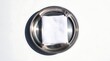 © MBAK NAH - Close-up shot of a stainless steel ashtray with a white napkin inside, on a white surface.