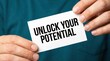 © Wajahat - Close up of a person holding a white card with the motivational phrase unlock your potential in bold black letters promoting self