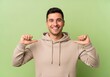 © PhotoHub - Young man wearing beige hoodie pointing at himself